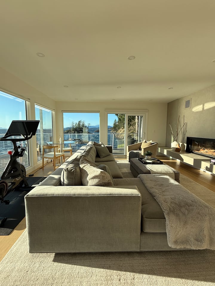 EagleView’s living space offers 180° ocean views, sofa, Peloton, bistro dining/work table, wood-burning fireplace, bar sink, mini fridge/freezer, microwave & coffee/tea station, plus large-screen TV, motorized blinds & hidden door to king bedroom.