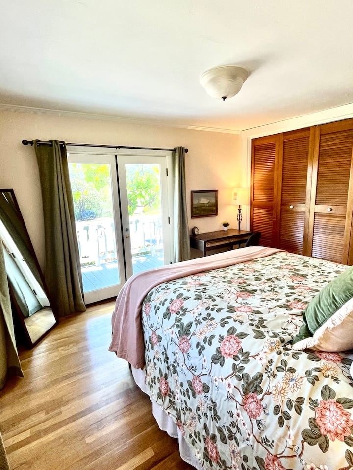 French doors and 2 windows offer tons of natural light and a view of the backyard pool. A full length mirror, desk, lamp, and chair complete the space. 