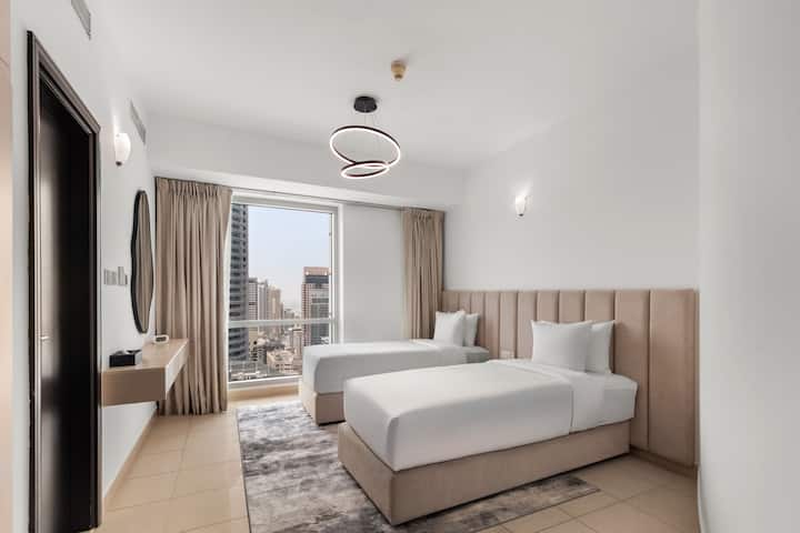 ️ 一间宁静的双床卧室，配备两张米色软垫床、洁白的床单和柔软的地毯。 大窗户让自然光线充足，同时展现窗外的城市风光，中性色调和现代照明营造出宁静、温馨的氛围。