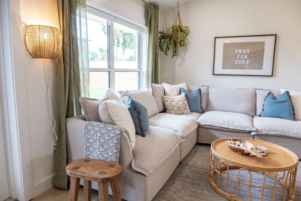 Living room with a cream sectional, rattan coffee table and garden windows
