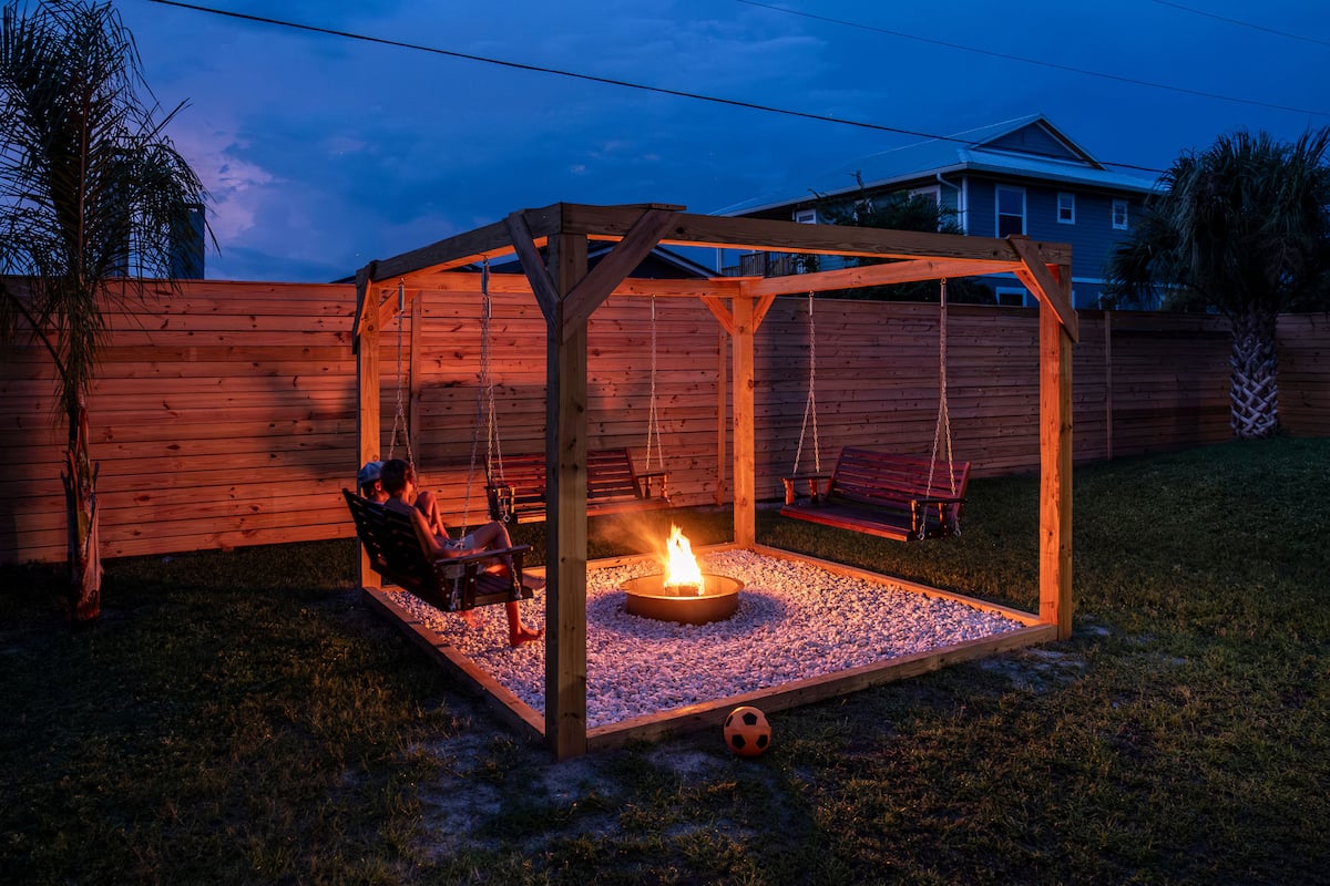 Pergola with swing benches around a glowing fire pit at dusk
