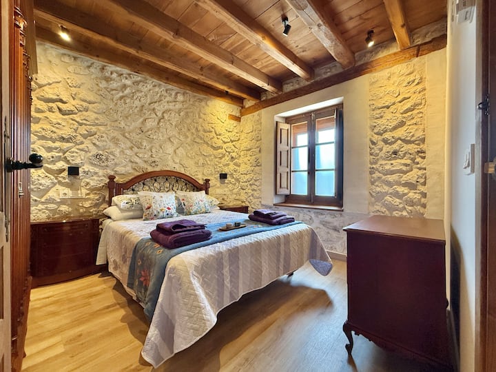 חדר שינה עם מיטה זוגית, קירות אבן ותקרת עץ שמספקים חום. חלל מואר ונוח, אידיאלי למנוחה אחרי יום של פעילויות באזור.