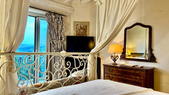 غرفة نوم رئيسية مع سرير بحجم كوين بأربعة أعمدة وتلفزيون وشرفة تطل على حمام السباحة والحديقة