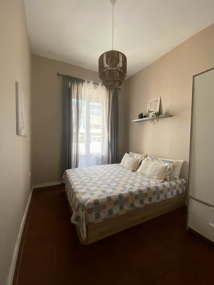 غرفة مع سرير 1.50 × 1.90 متر مع مرتبة مرنة، وطاولتان، وخزانة، وموقد، وتكييف هواء محمول في الصيف وطاولة عمل.