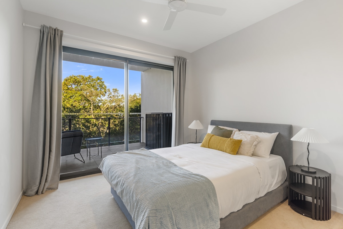 استرخ في سرير أنيق بحجم كوين مع أبواب زجاجية منزلقة تفتح على شرفة تطل على محيط هادئ ووريق.