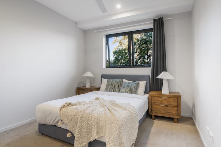 Relájate en una elegante cama tamaño queen con ventanas que invitan a la abundante luz natural, complementada con sábanas de estilo hotelero y almohadas mullidas.