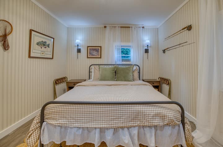 A spacious queen-sized bed with two gel pillows and two plush pillows, and a cotton duvet. A window AC unit that provides extra cool air in the summer months. Two night stands on either side and two luggage racks for guest use.