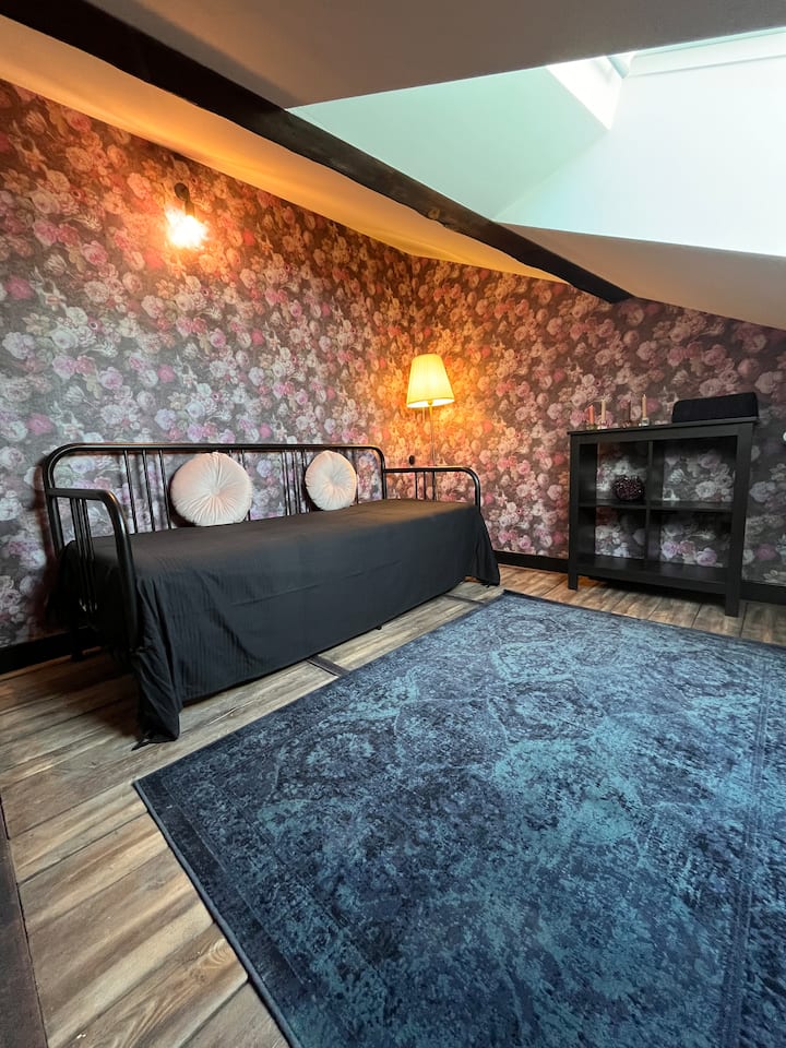 Mala dodatna spavaća soba ispod krova s novim kaučem na razvlačenje, podnom svjetiljkom i policom.