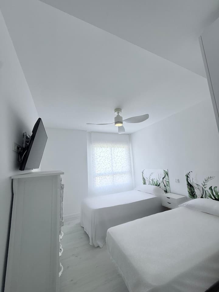 Спална соба со поглед кон базен и зелени површини. Има паметен телевизор