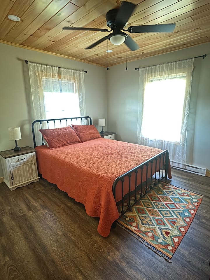 غرفة نوم مجهزة بسرير بحجم كوين ومروحة سقف ومكيف سبليت صغير للتدفئة أو التبريد وحمام داخلي كامل.