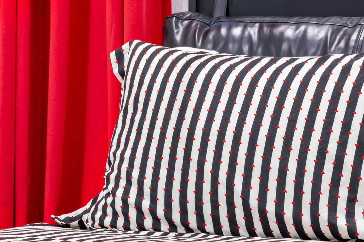 一张卧室的时尚细节照片，配有大胆的条纹床上用品，红色的装饰与红色的窗帘相映成趣