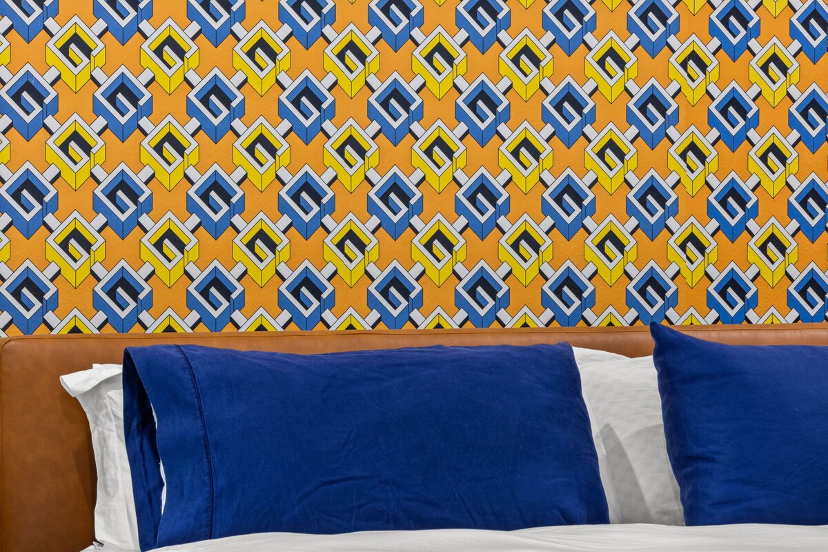 充满活力的卧室，采用正宗的Gucci几何图案墙纸、丰富的蓝色装饰和舒适的床铺，是时尚与舒适相结合的空间。