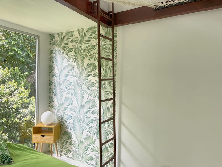 La cama se encuentra en una acogedora zona de loft accesible por una escalera. El espacio está diseñado solo para el colchón, creando un lugar íntimo y único para descansar. También hay una red de cuerda estilo hamaca donde puedes relajarte y descansar.