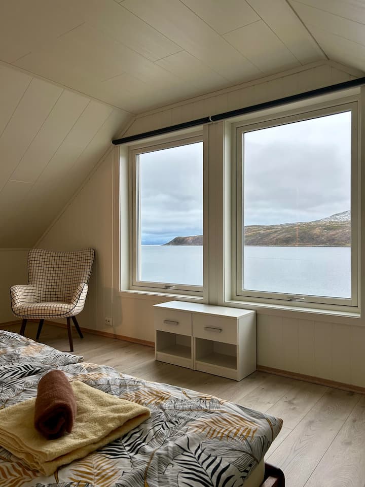 18 m² bedroom with double bed, large windows, wardrobe with stunning sea and mountain views. Bright, minimalist design with comfortable armchair and soft bedding.