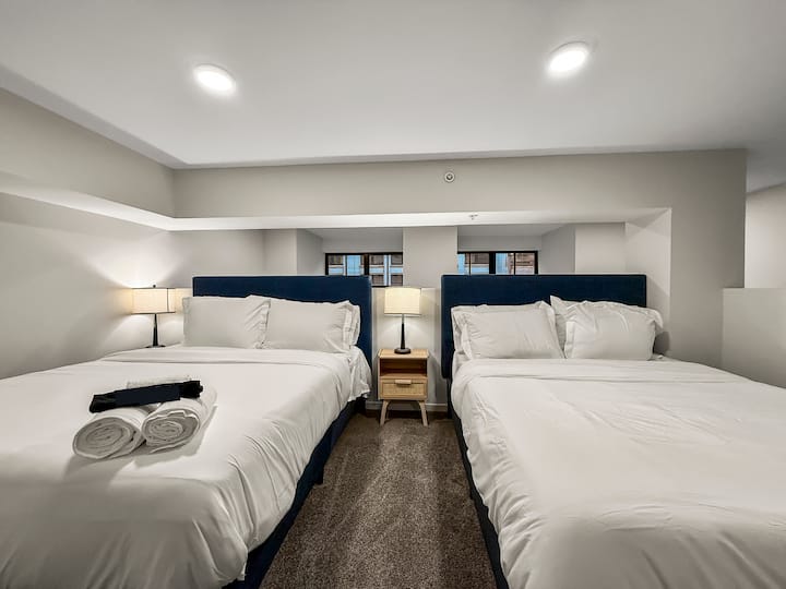 Уютна самостоятелна спалня с плюшени двойни легла, меки чаршафи и стилно градско докосване, за да се осигури комфортна нощна почивка.