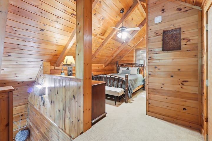 Manželská posteľ s lavičkou na sedenie a komodou v podkroví.