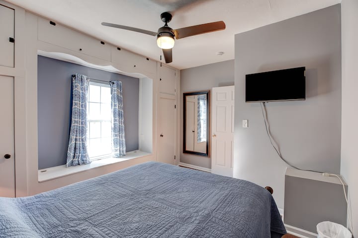 Lit queen avec une table de nuit au niveau principal. Ventilateur de plafond et petite télévision avec Amazon Fire Stick. 