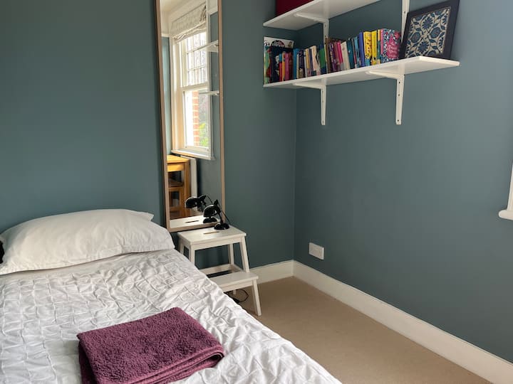 החדר הקטן ביותר עם מיטת יחיד, חלון גדול, מתלה בגדים ושולחן קטן. 