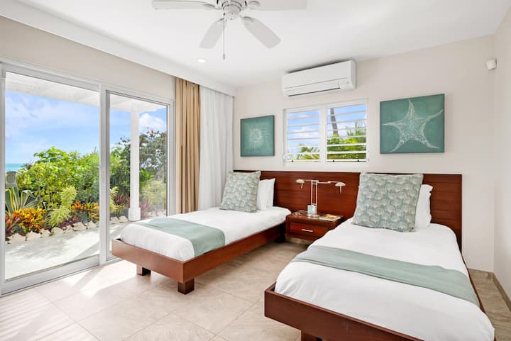 Dormitorio en el nivel inferior con 2 lujosas camas individuales y acceso directo a la terraza, la terraza principal y la playa de arena más allá. Ideal para niños o huéspedes individuales.