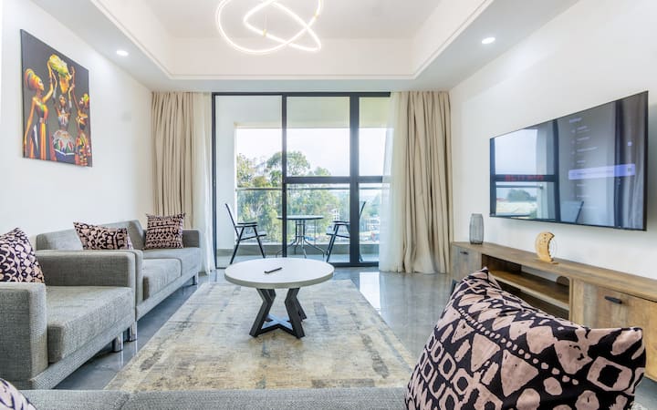 Elegantan dnevni boravak s trosjedom i dvosjedom s mekanim jastucima, 55-inčnim Samsung televizorom, okruglim krem stolom za kavu, kutnim stolcima i ručno tkanim tepihom koji unosi toplinu i stil u udoban moderan prostor.