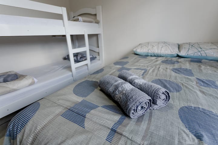 Quarto 2 prontinho pra família: cama de casal + beliche, com roupa de cama e toalhas já separadas.