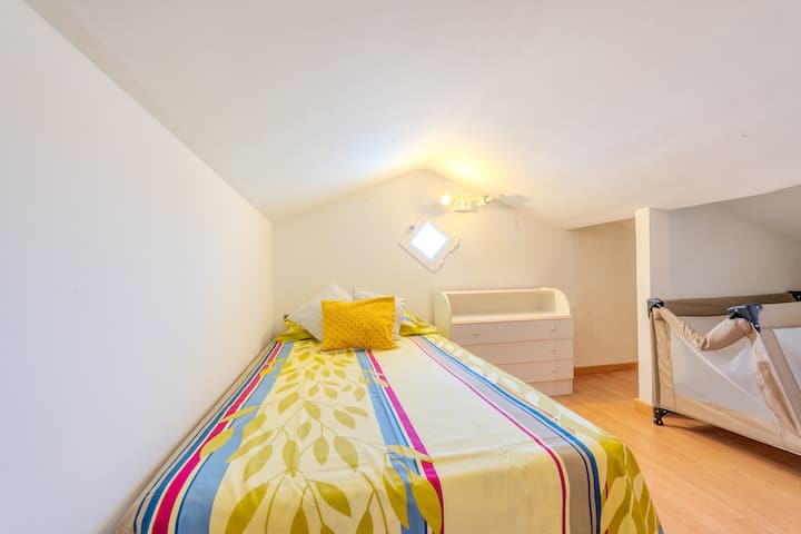 Dormitorio 5 con cama individual y colcha de colores bajo el techo inclinado: alegre y luminoso.