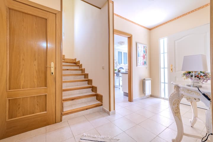 Recibidor con escalera y consola clásica: bienvenida amplia y luminosa a la villa.