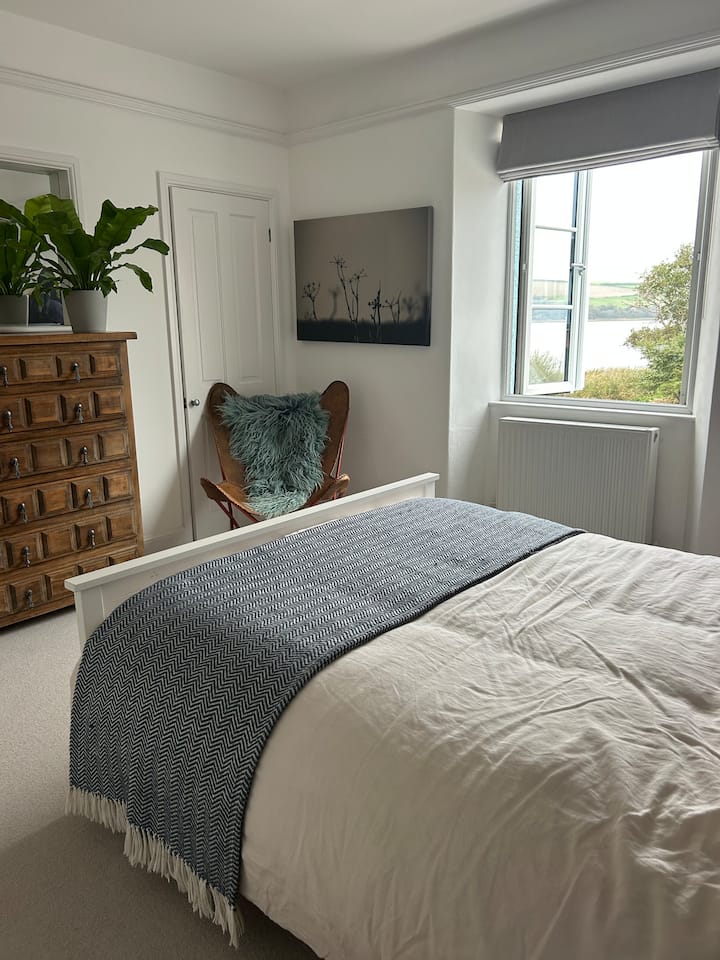 Un dormitorio espacioso con cama tamaño king.  Las ventanas dobles se abren a una vista del Ley/duckpond a la izquierda con el paseo marítimo a la derecha.