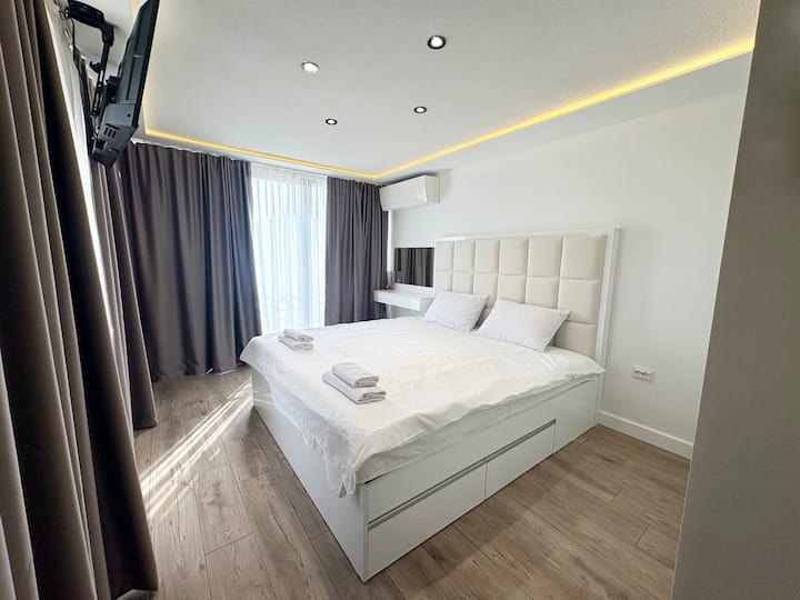 Prostrana spavaća soba s velikim krevetom, ormarom i toaletnim stolićem. Francuski prozori osiguravaju prirodno svjetlo, a televizor i klima-uređaj pružaju udobnost, stvarajući ugodan i funkcionalan prostor za opuštanje.