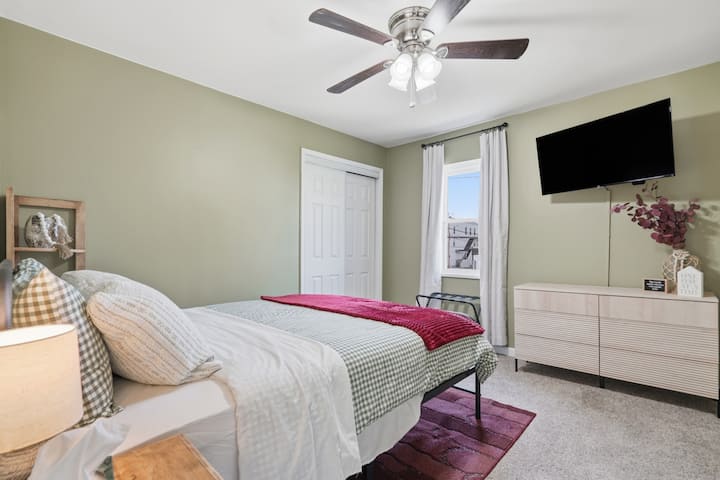 Comfortable bedroom featuring a cozy bed, TV, and dresser for storage. Includes a closet with hangers, iron, phone charging outlets by the bed, and an optional pack ’n play—perfect for families or longer stays.