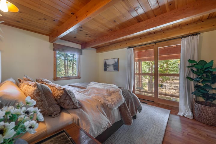 Relajante dormitorio principal con cama tamaño king con ropa de cama lujosa, techos de madera cálida y acceso directo a la terraza rodeada de árboles.