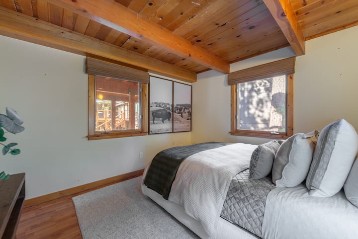 Cómodo dormitorio tamaño queen con sábanas suaves, techos con vigas de madera y luz tranquila del bosque.