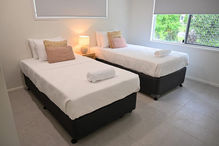 Relax in a comfortable bedroom featuring soft lighting, simple furnishings, and plush beds. Large windows bring in gentle daylight, creating a cozy, restful atmosphere where you can unwind, settle in, and wake up feeling refreshed during your stay.