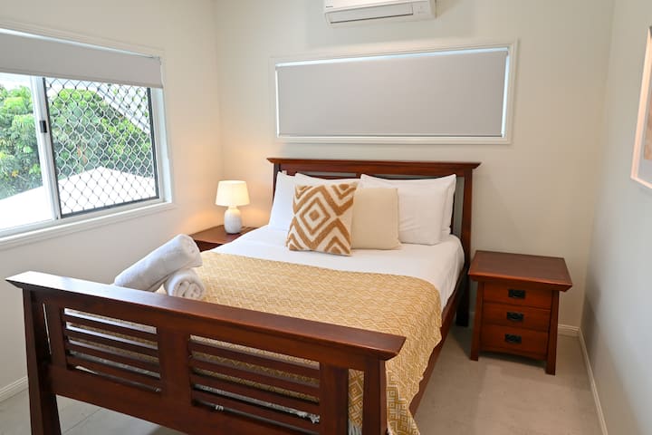 Relax in a comfortable bedroom featuring soft lighting, simple furnishings, and a plush bed. Large windows bring in gentle daylight, creating a cozy, restful atmosphere where you can unwind, settle in, and wake up feeling refreshed during your stay.