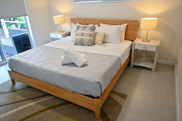 Relax in a comfortable bedroom featuring soft lighting, simple furnishings, and a plush bed. Large windows bring in gentle daylight, creating a cozy, restful atmosphere where you can unwind, settle in, and wake up feeling refreshed during your stay.