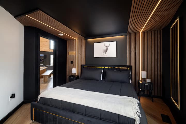 Bedroom 2 with a king-size bed, modern black walls, warm wood slat accents, soft accent lighting, bedside tables, and a stylish cabin-inspired design.