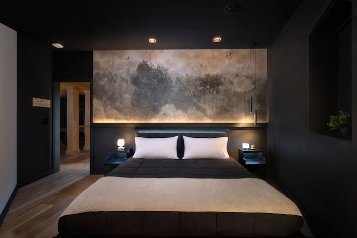 Bedroom 5 with a king-size bed, dark modern walls, warm accent lighting, scenic wall art, bedside tables, and a cozy luxury cabin-style atmosphere.