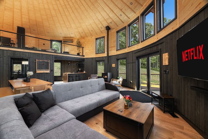 Bright open living room with sectional sofa, large TV, Netflix, Disney, HBO, soaring wood ceiling, tall windows, dining area, kitchen, loft views, and warm modern cabin-style finishes.