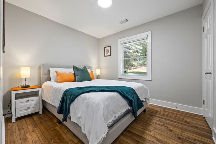 Светла спалня за гости с двойно легло, меки лампи и дървени подове.Щорите на прозорците създават настроение, а гардеробът поддържа чантите подредени.