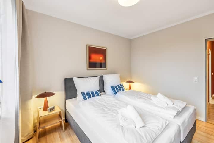 Светла спалня в меки бежови тонове с две удобни единични легла (могат да бъдат свързани и като двойно легло). Достъп до балкона с изглед към зеленина, стилно осветление и модерен дизайн за добър сън.