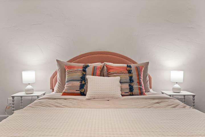 เตียงควีนไซส์ที่สะดวกสบายพร้อมหัวเตียงสีชมพูที่ดูสนุกสนานช่วยเพิ่มสีสันและเสน่ห์ให้กับห้อง