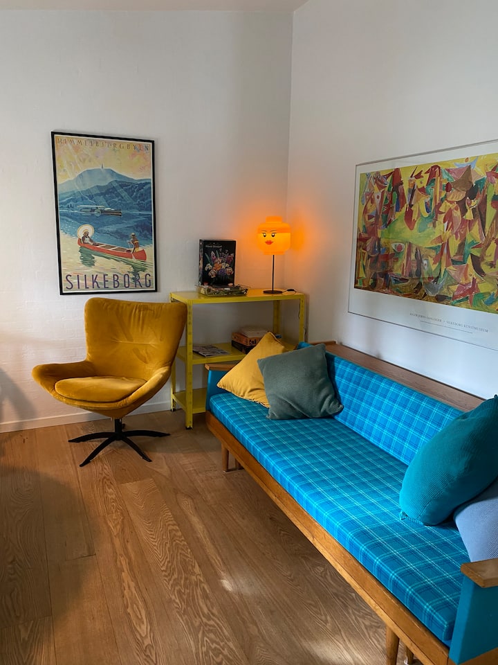 El salón contiene un sofá cama con nido, una zona de comedor, un sillón y un armario. También hay algunos juegos de mesa y libros.