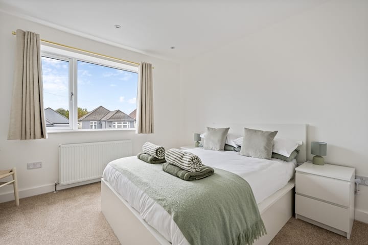 Bright double bedroom with crisp white linens, soft sage throw and fresh towels ready on arrival. A large window brings in daylight and the calm, minimalist styling makes it perfect for couples, friends, or longer stays.
