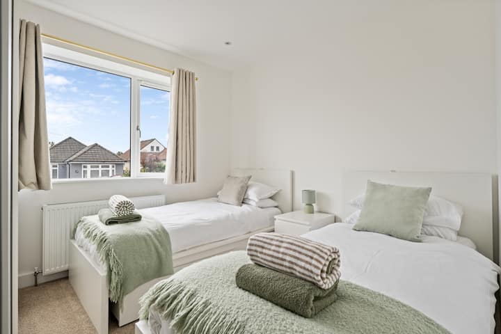 Bright twin bedroom with two comfortable single beds, crisp white linens and soft sage throws. Fresh towels are provided and the large window brings in daylight, making it ideal for kids, friends, or extra guests.
