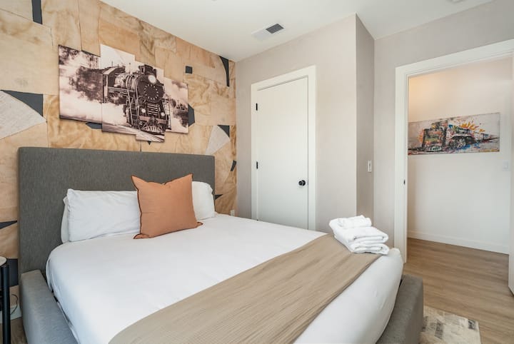 Stylish king bedroom with balcony views, modern art accent wall, plush bedding, and natural light—comfortable, quiet, and perfect for a relaxing stay.