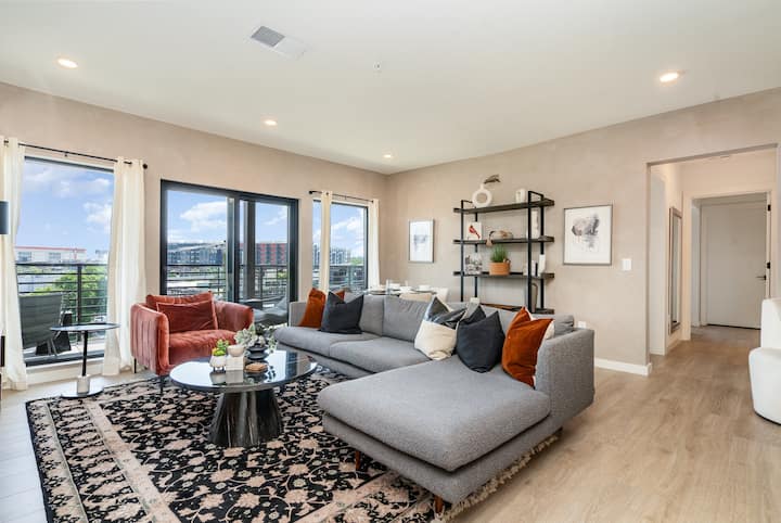 Spacious, stylish living room with sectional sofa, designer decor, and balcony views—perfect for relaxing, entertaining, or enjoying city sunsets.