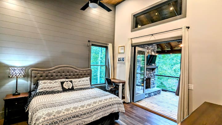 Wake up surrounded by the forest — this serene master suite blends rustic warmth with modern elegance, featuring high ceilings, natural light, and peaceful woodland views