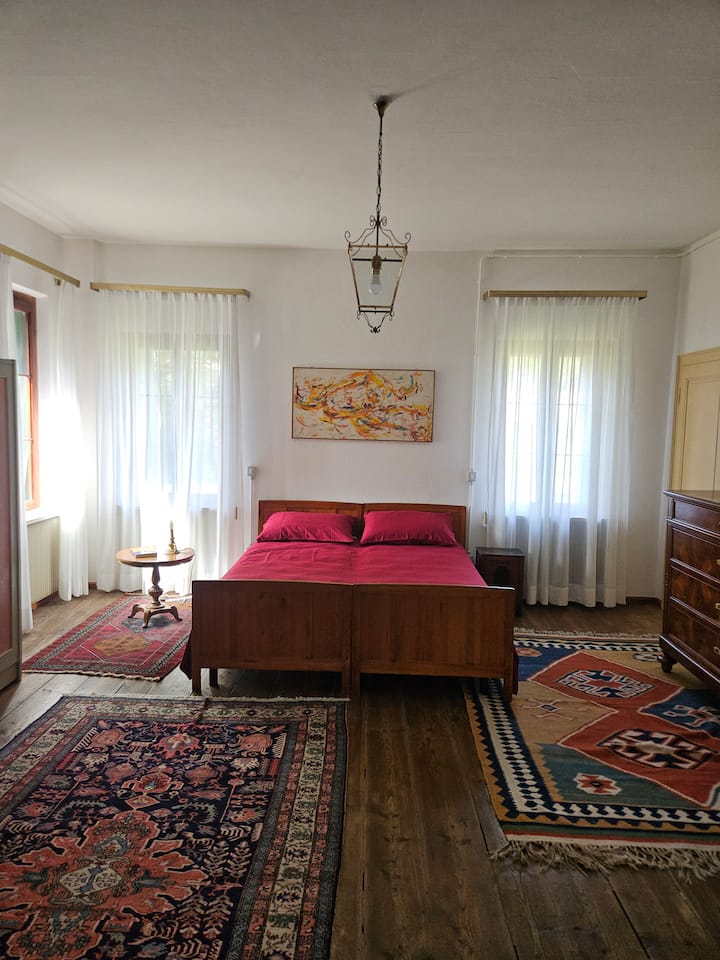 חדר שינה מרווח ובהיר עם מיטה זוגית מעץ וכיסוי מיטה אדום חם שנותן מגע של חיים לסביבה.