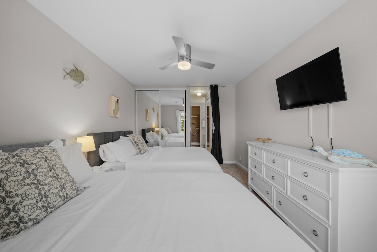 غرفة نوم هادئة في الطابق الرئيسي مع سريرين فخمين بحجم كوين وبياضات جديدة وألوان ساحلية هادئة.