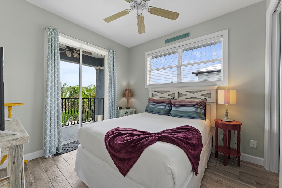 חדר שינה עם מיטת קווין סייז למעלה עם מרפסת ונוף חלקי למפרץ, טלוויזיה וחדר ארון. 